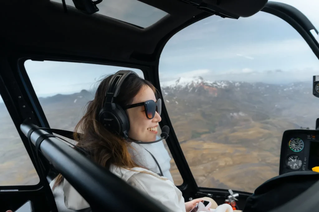 Woman wearing headphones and sunglasses inside a helicopter flying over the rugged volcanic landscape of Landmannalaugar in Iceland.