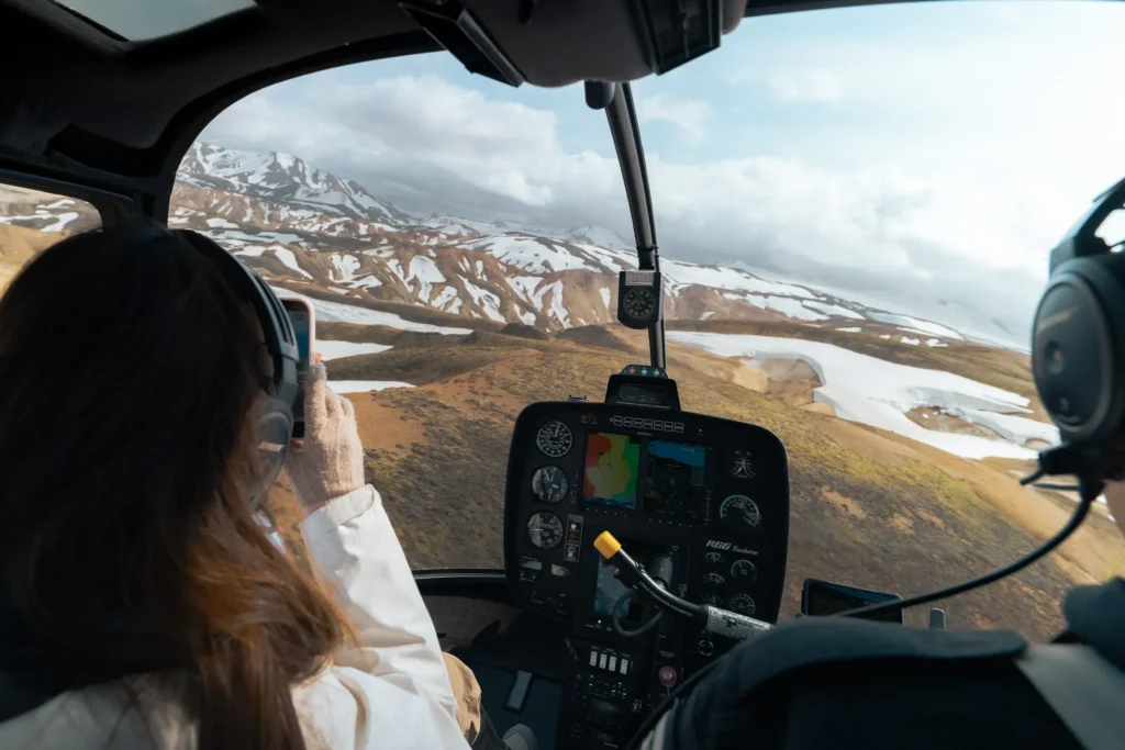 Woman photographing the snow-covered volcanic mountains of Landmannalaugar from inside a helicopter in Iceland.