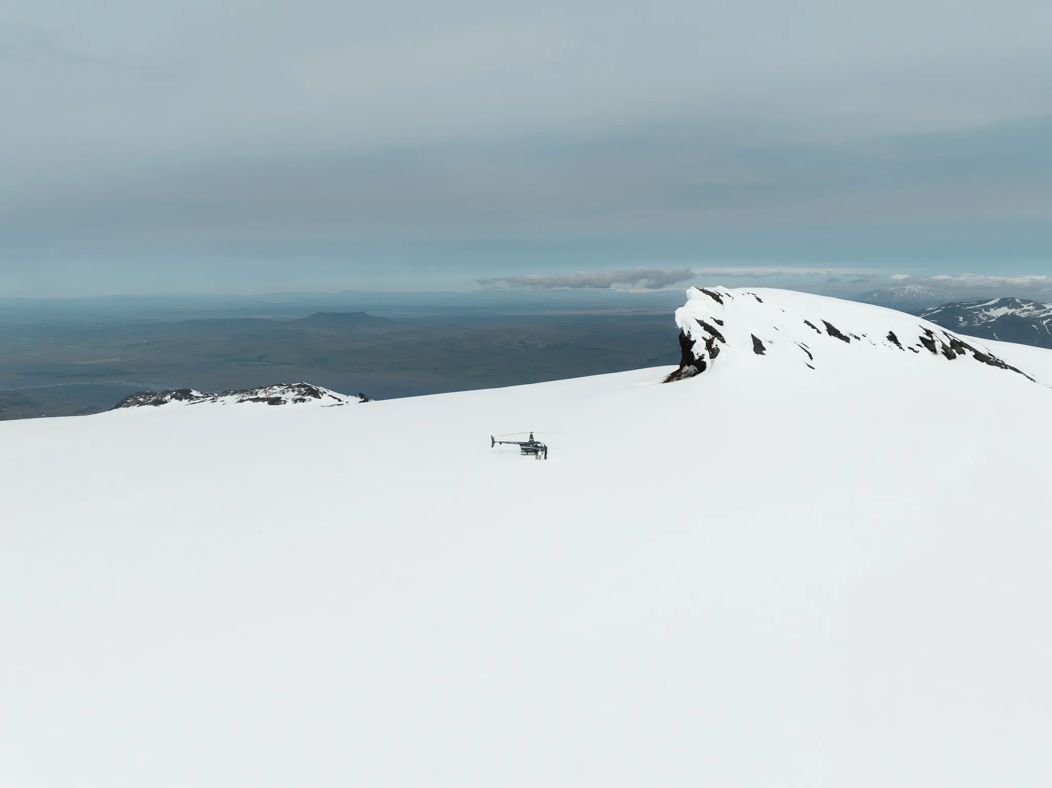 Helicopter resting on a snow-covered glacier during a proposal beneath a mountain peak in Iceland.