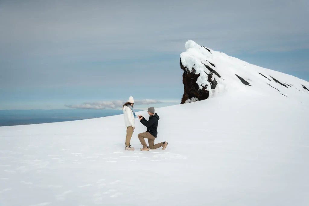 A man proposing to his partner on a snowy glacier in Iceland, with a dramatic snow-covered mountain in the background.