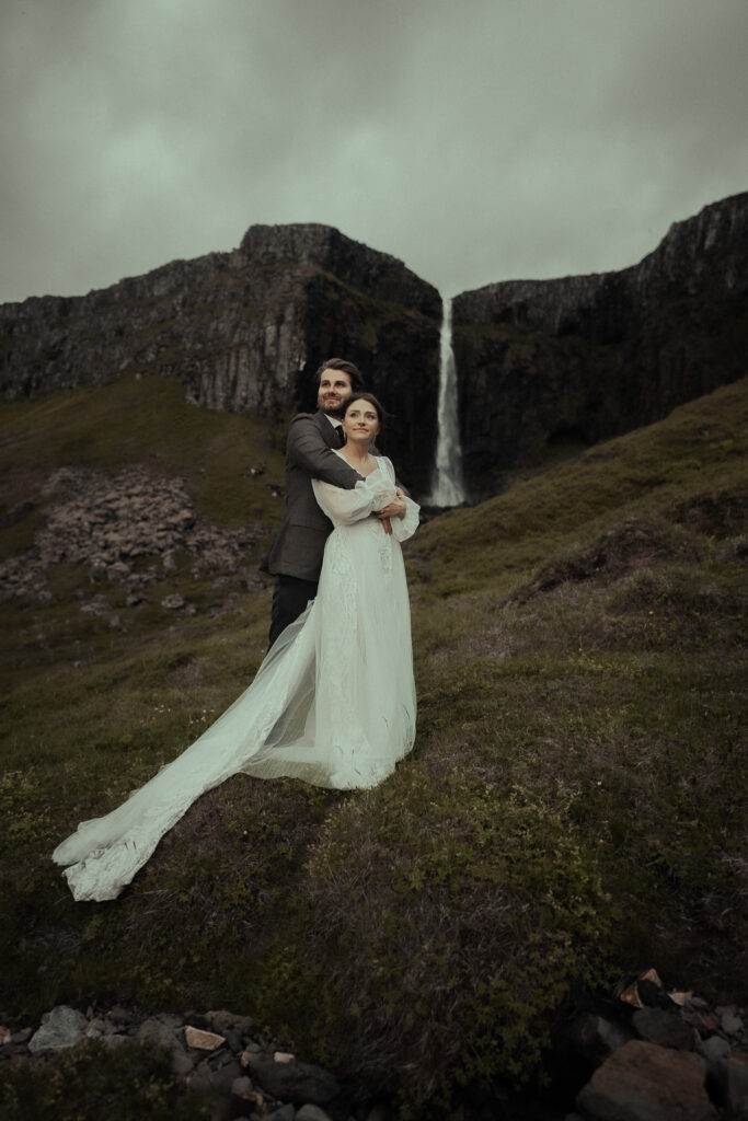 A bride and groom embracing in front of a waterfall near Grundarfoss in Iceland