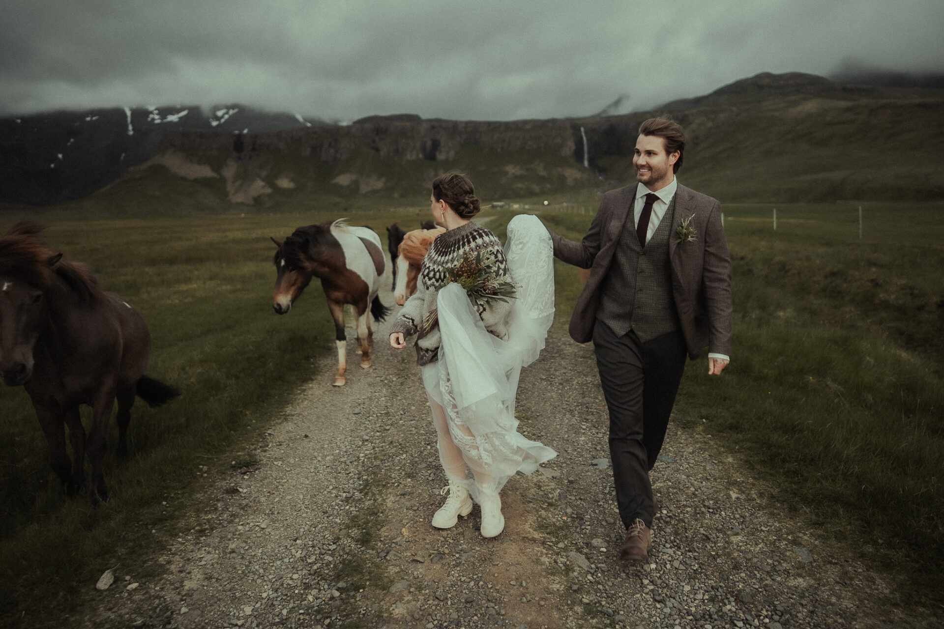 A bride and groom walking along a gravel road with Icelandic horses near Grundarfoss in Iceland