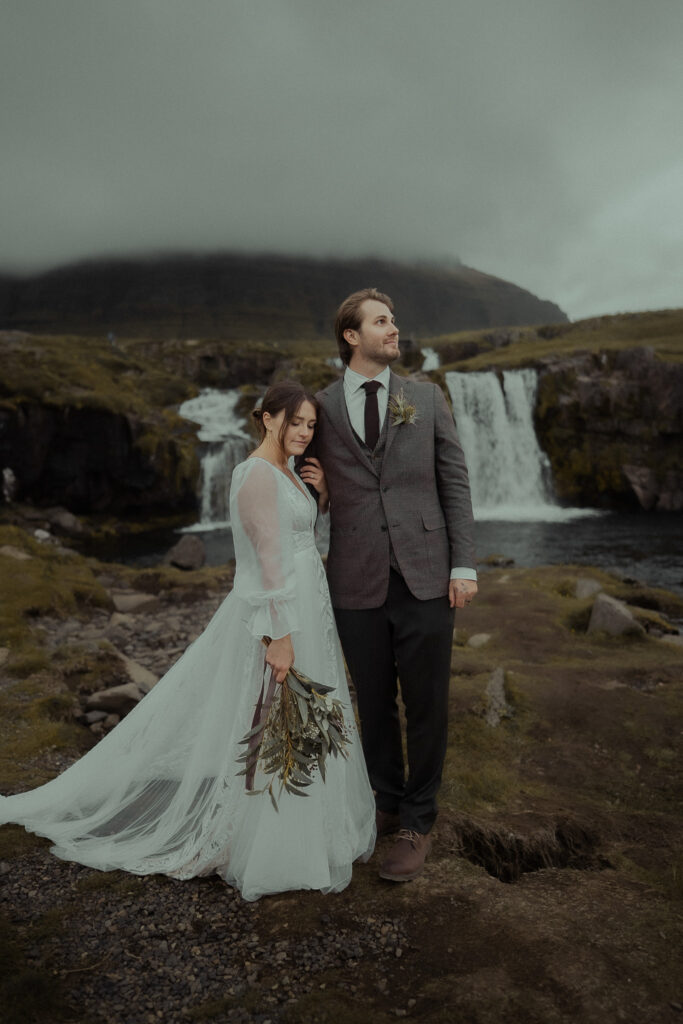 A bride and groom standing together near waterfalls at Kirkjufell in Iceland
