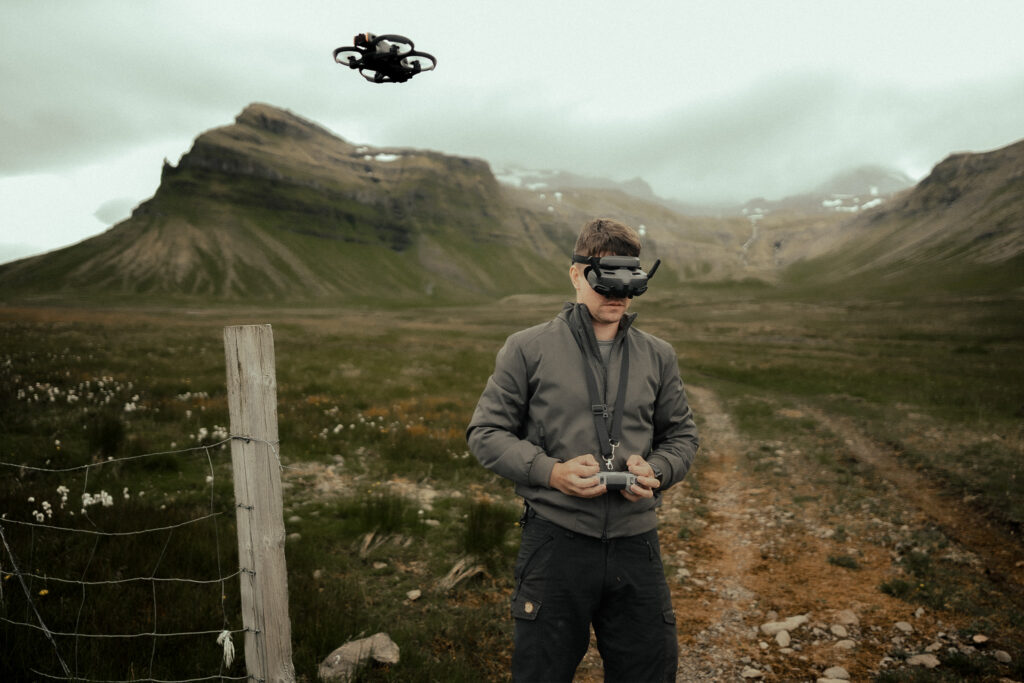 A drone pilot wearing FPV goggles flying a quadcopter in a mountainous landscape in Iceland
