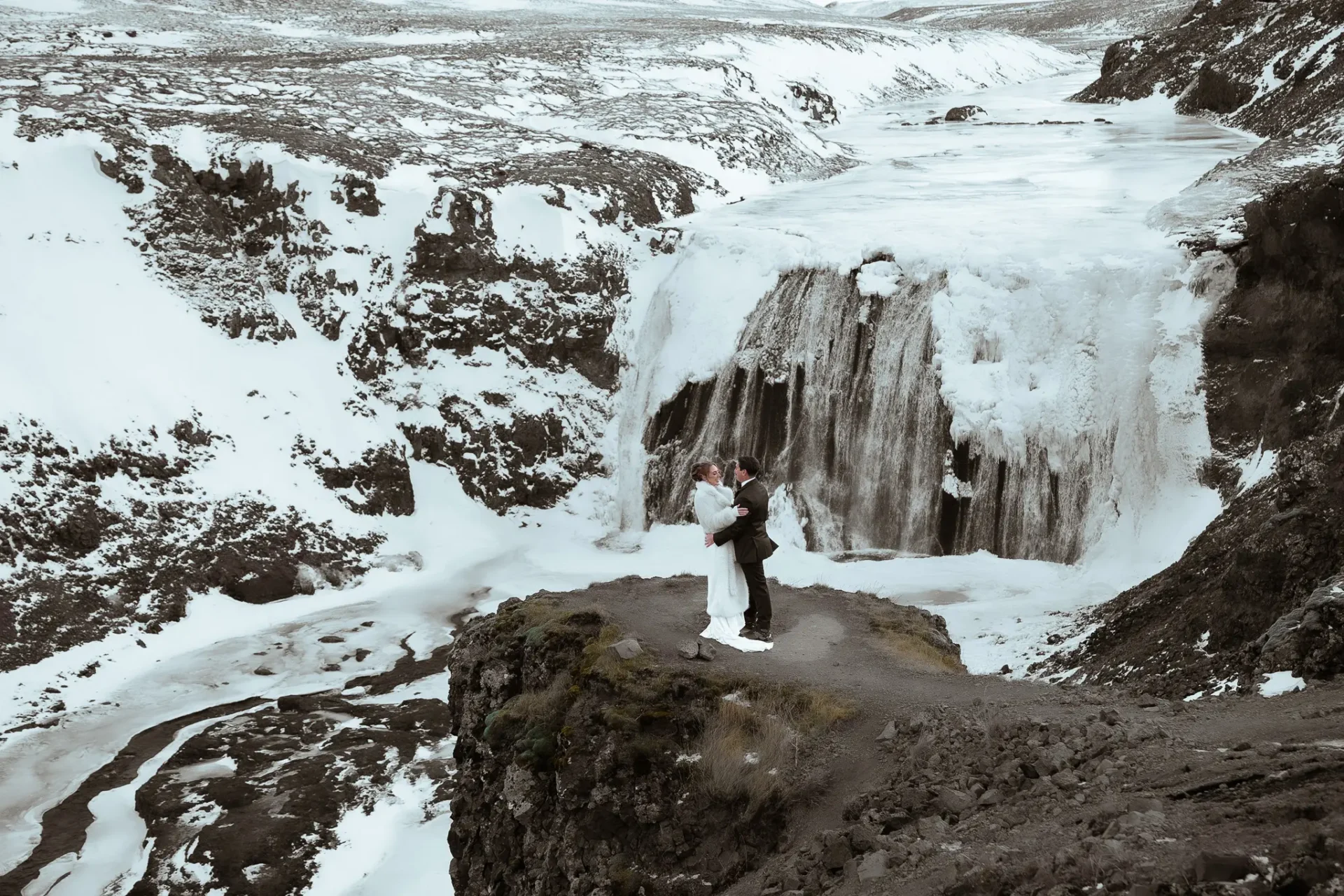 Bride and groom embracing in front of a frozen Þórufoss waterfall in Iceland