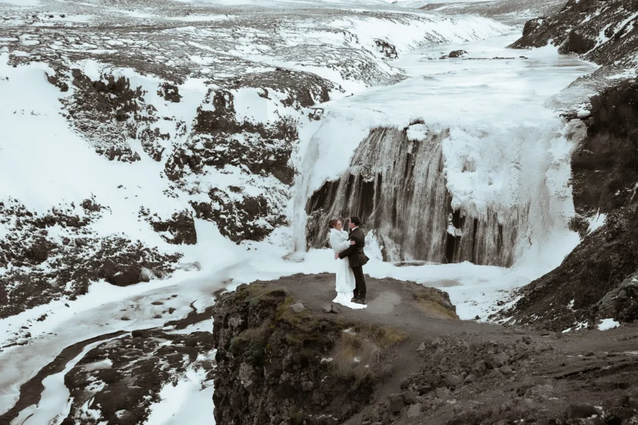 Bride and groom embracing in front of a frozen Þórufoss waterfall in Iceland