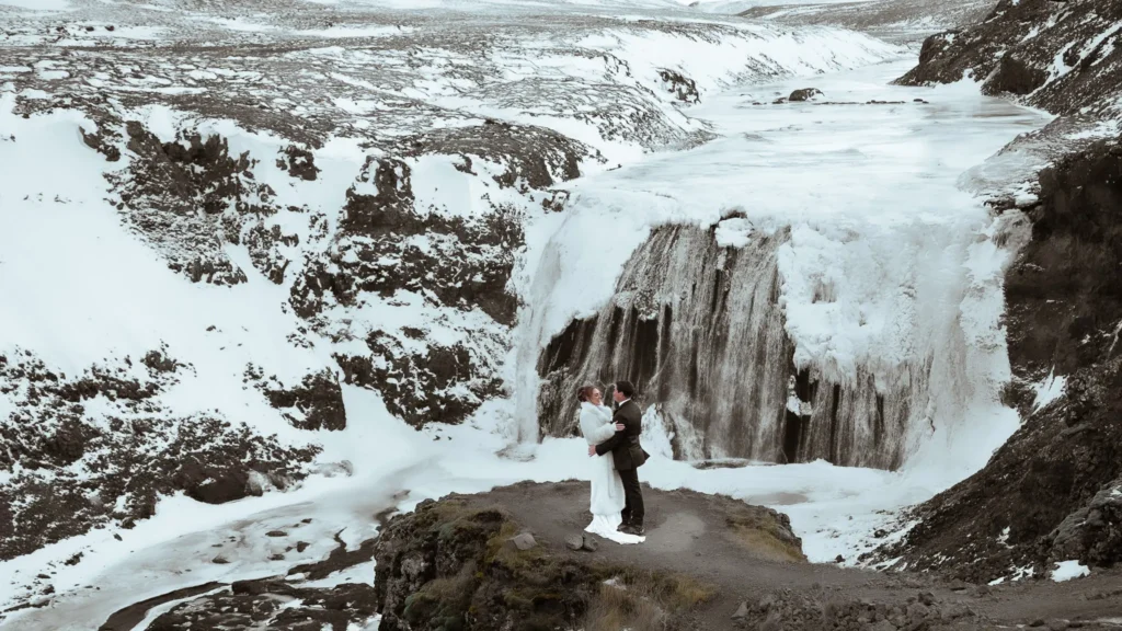 Bride and groom embracing in front of a frozen Þórufoss waterfall in Iceland