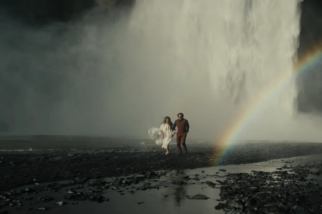 An elopement couple running in front of Skógafoss waterfall with a rainbow in the mist
