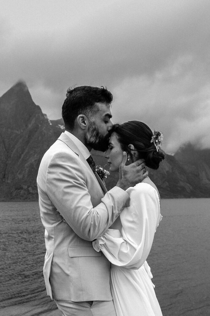 Intimate black and white elopement portrait of a groom kissing his bride by the sea in the Lofoten Islands