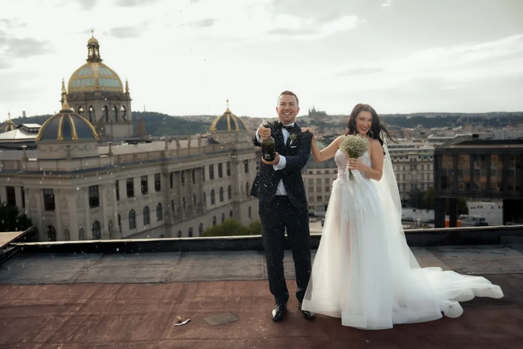 Bride and groom celebrating with champagne on a rooftop overlooking Prague