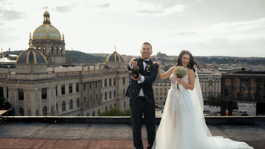 Bride and groom celebrating with champagne on a rooftop overlooking Prague