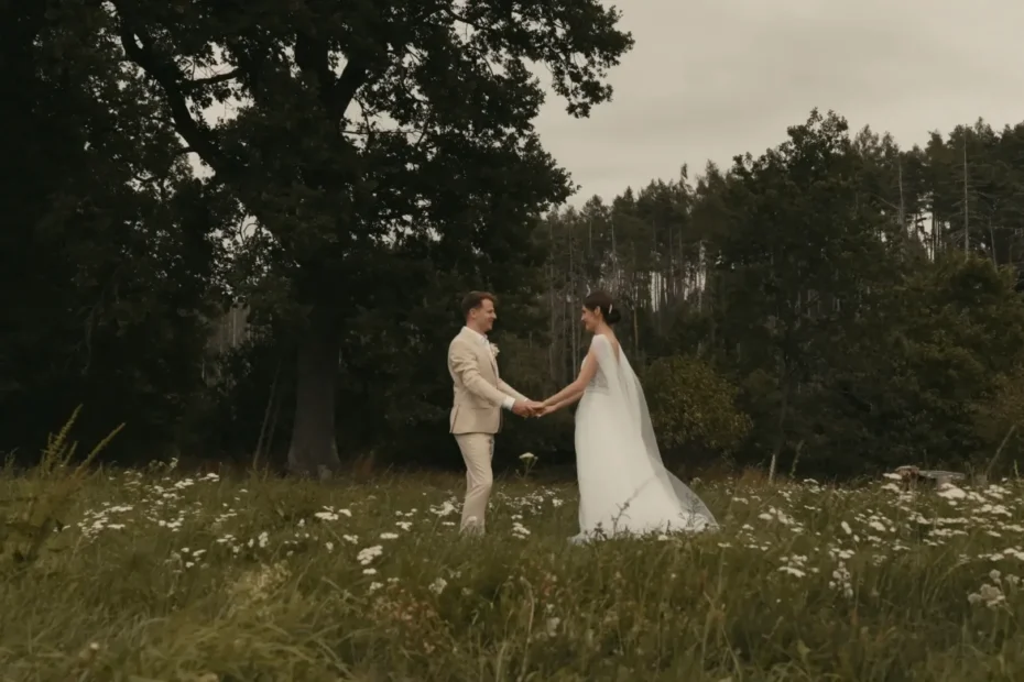 Nevěsta a ženich se drží za ruce na louce plné divokých květin se stromy v pozadí