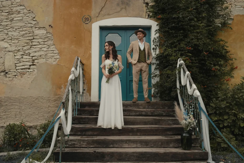 Nevěsta a ženich na dřevěných schodech před rustikálním kamenným domem ve svatebním místě Na Lisu