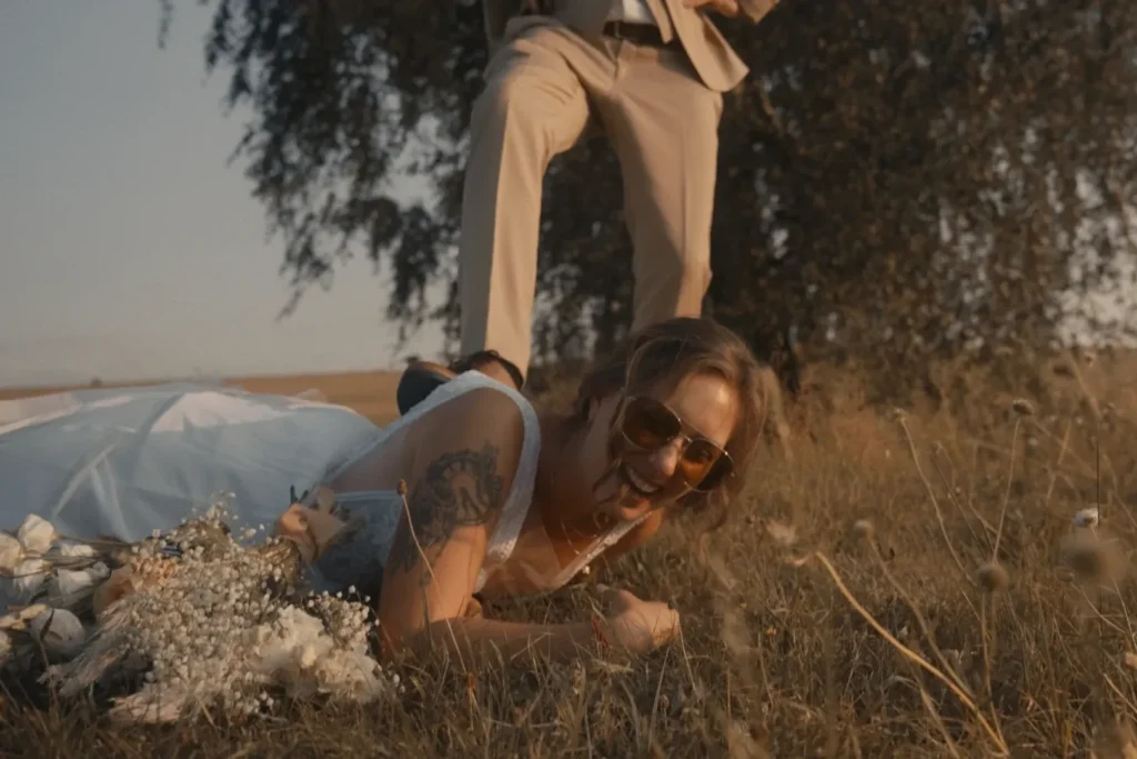 Nevěsta leží na zemi a směje se, zatímco ženich žertovně pózuje s jednou nohou blízko ní