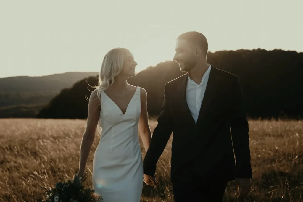 Nevěsta a ženich kráčejí polem při západu slunce